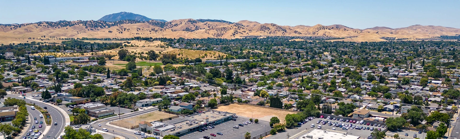
Drone photo over a neighborhood in Antioch, California with houses, commercial buildings and a blue sky 