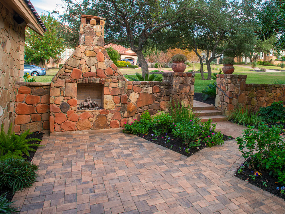 Outdoor fireplace, pavers, outdoor kitchen, BBQ, grilling station, outdoor lighting, retaining wall, artificial turf, cozy, fire, lit, paver patio, patio furniture, outdoor living, total outdoor transformation, backyard, fire, paving stones, sunset, universal region, evening