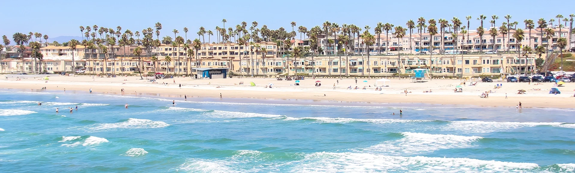 View of the beach in Oceanside, California. Bright blue water and homes in the background. 