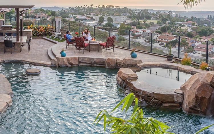 Couple enjoys view by the pool. Elevated paving stone patio with incredible view and stone pool deck, hot tub and built-in kitchen. 