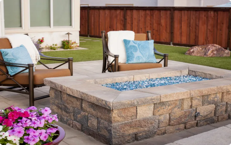 Built-in paver firepit on paver patio with chairs and flowers