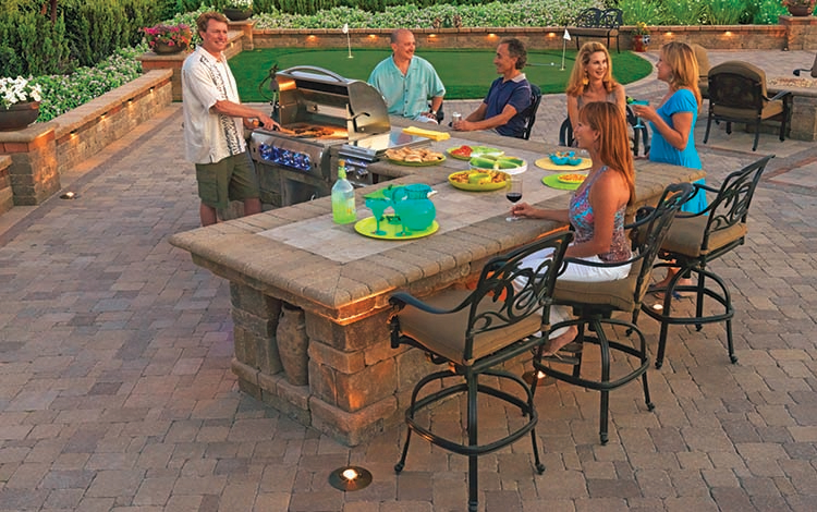 Outdoor kitchen on paver patio with people enjoying a party. 