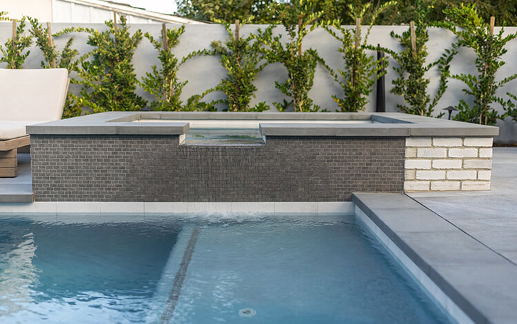 Hot tub over pool with stone pool deck and stone wrap. Modern gray pool deck in California. 