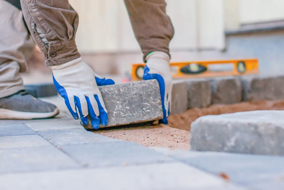 Construction team member placing a paver block by hand with precision, showcasing craftsmanship, attention to detail, and pride in quality work.