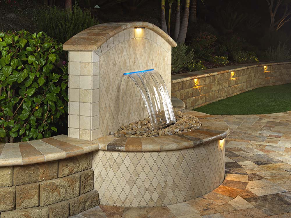Water fountain with paving stone retaining wall, outdoor lighting and artificial turf lawn