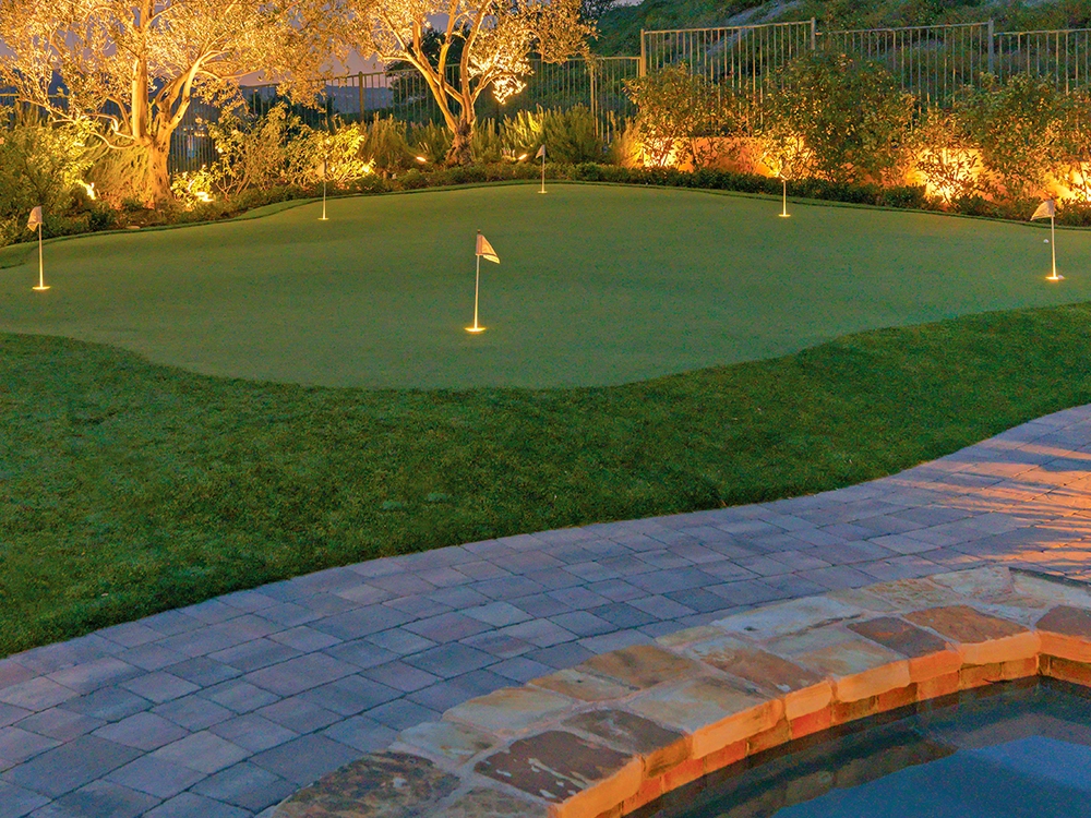 Putting green in a backyard in Atlanta with amazing lighting and a paving stone pool deck. 