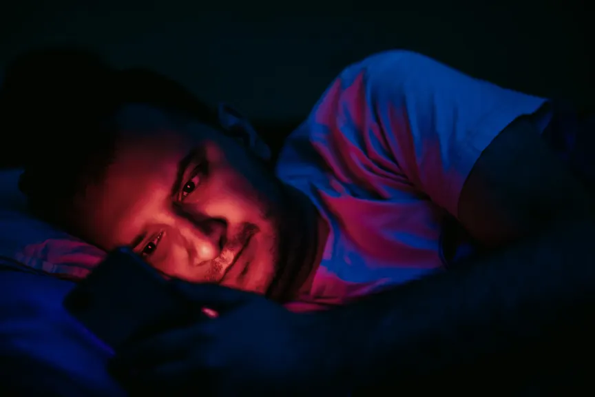 Man laying in bed while looking at his phone