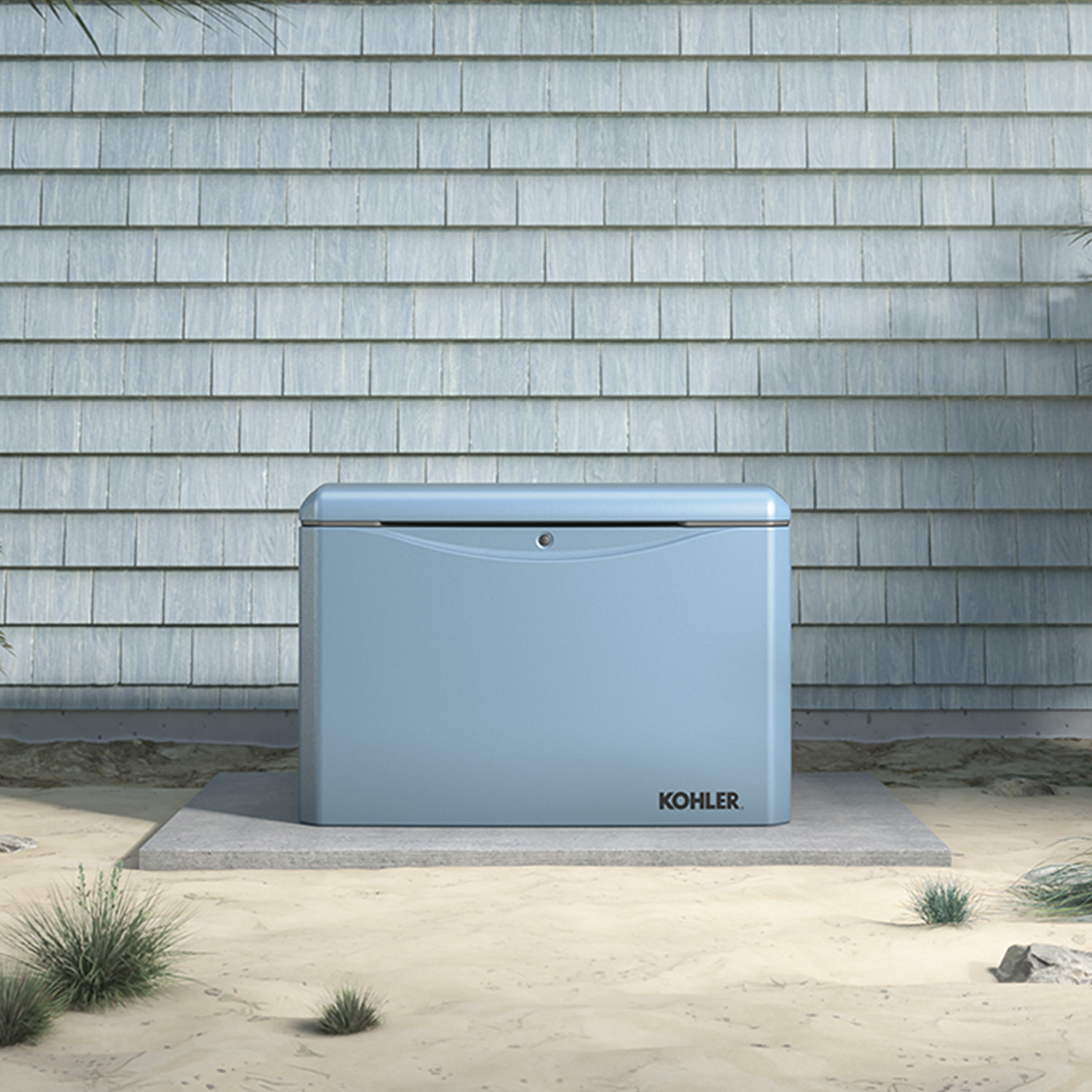 Image of a Canyon Blue colored Kohler Home Generator outside of a house standing on a cement base in a sand area with a small palm tree in background