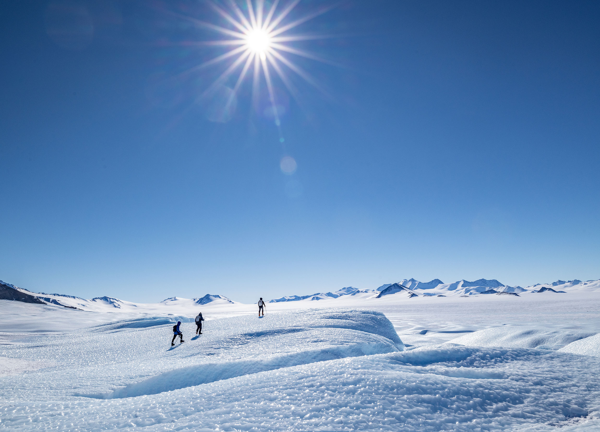 Image of blue ski, open mountain range covered with snow and 3 skiers
