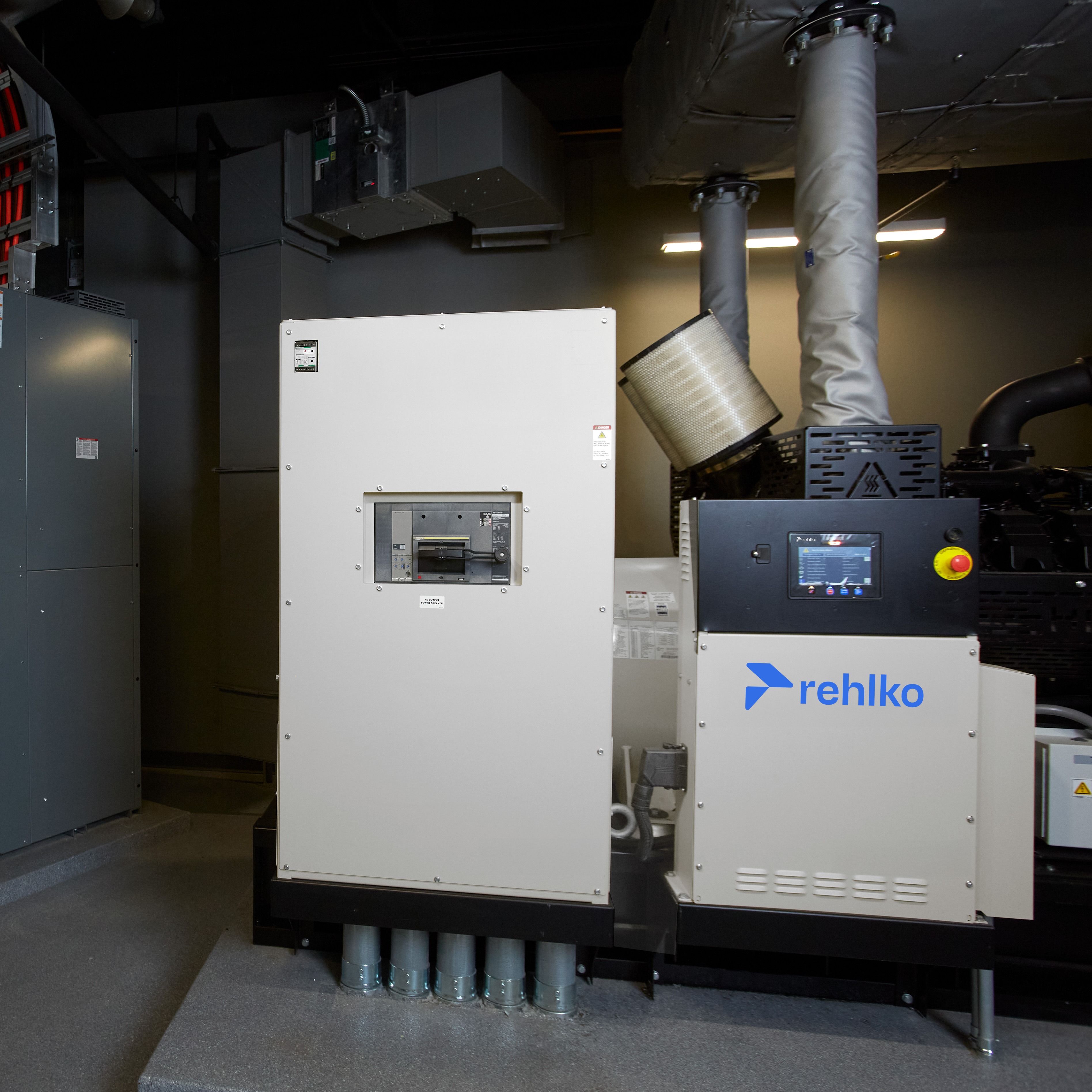 Controllers and generators inside a dark machinery room, surrounded by industrial equipment and low lighting.