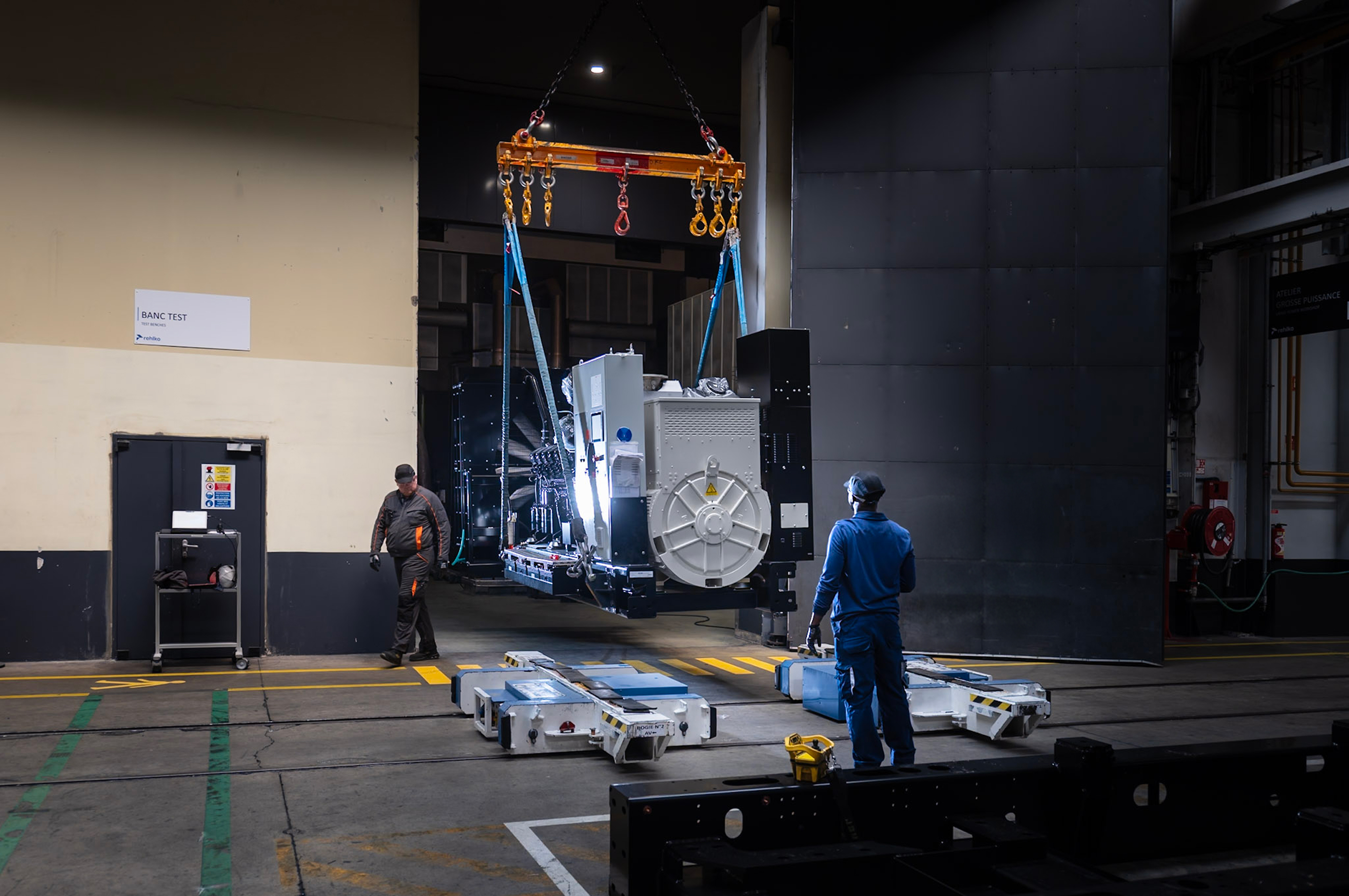Industrial generator being crane-lifted during factory testing and commissioning in a manufacturing facility.