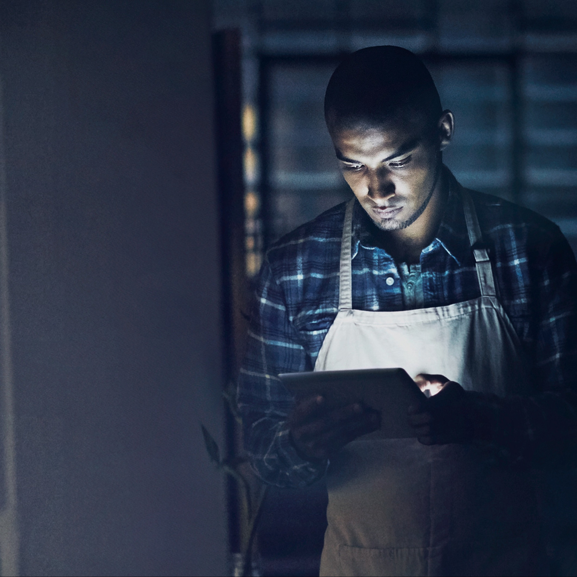 Man in a dark room looking at a tablet; small business