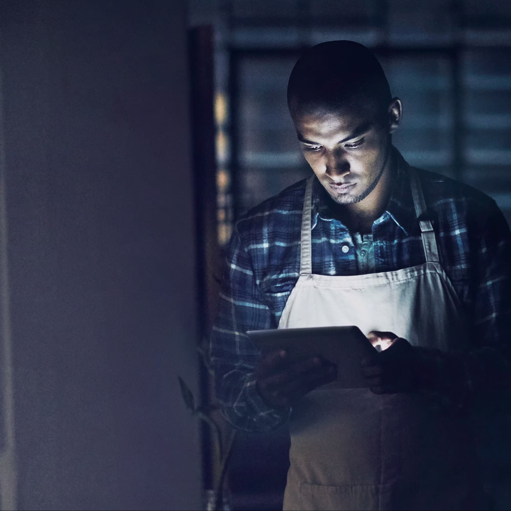 Man in a dark room looking at a tablet; small business