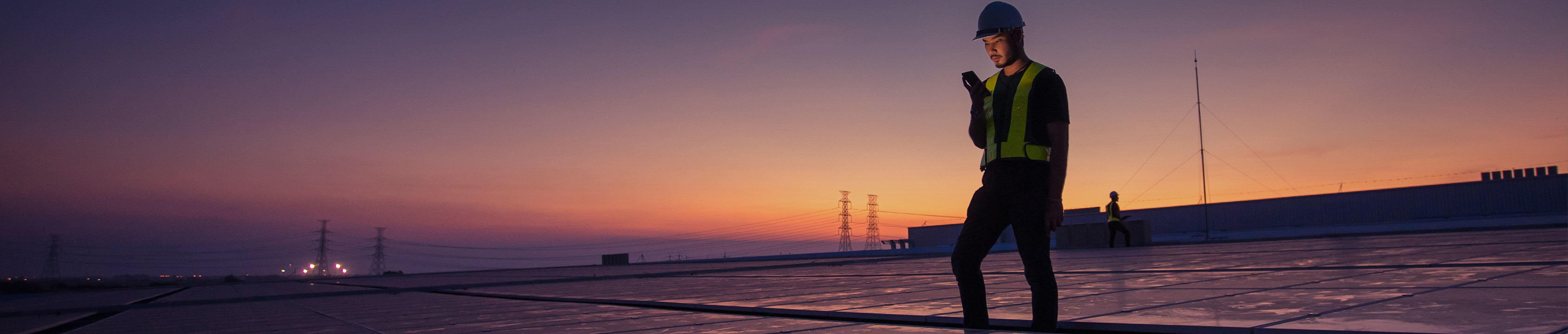 Tecnico che cammina in un impianto solare commerciale al tramonto, simbolo di energia rinnovabile, riduzione delle emissioni, operazioni sostenibili e strategie di decarbonizzazione a lungo termine.