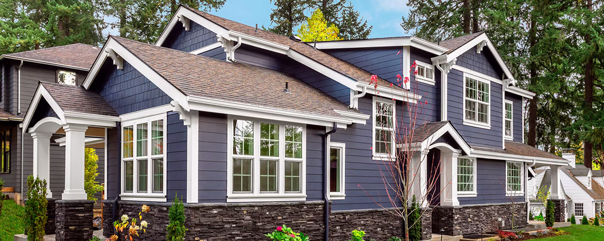 Charming gray house featuring a porch, gray siding, and white trim details, nestled among lush green trees.