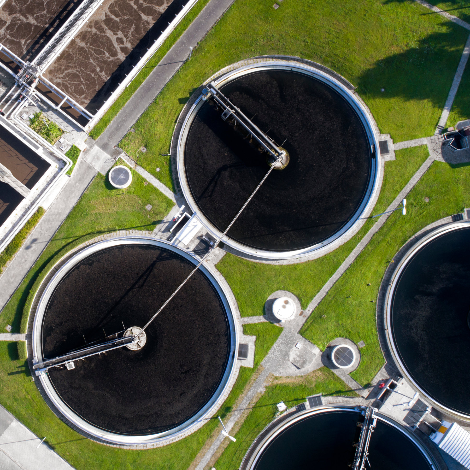 Aerial drone photo of a wastewater treatment plant showing large circular clarifiers, tanks, and surrounding infrastructure.