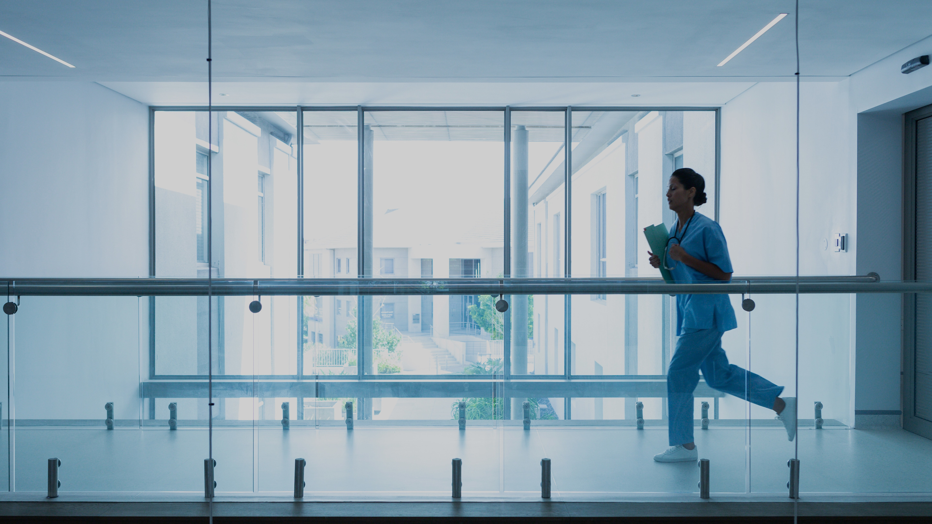 Woman in scrubs running inside a hospital building with all-glass windows