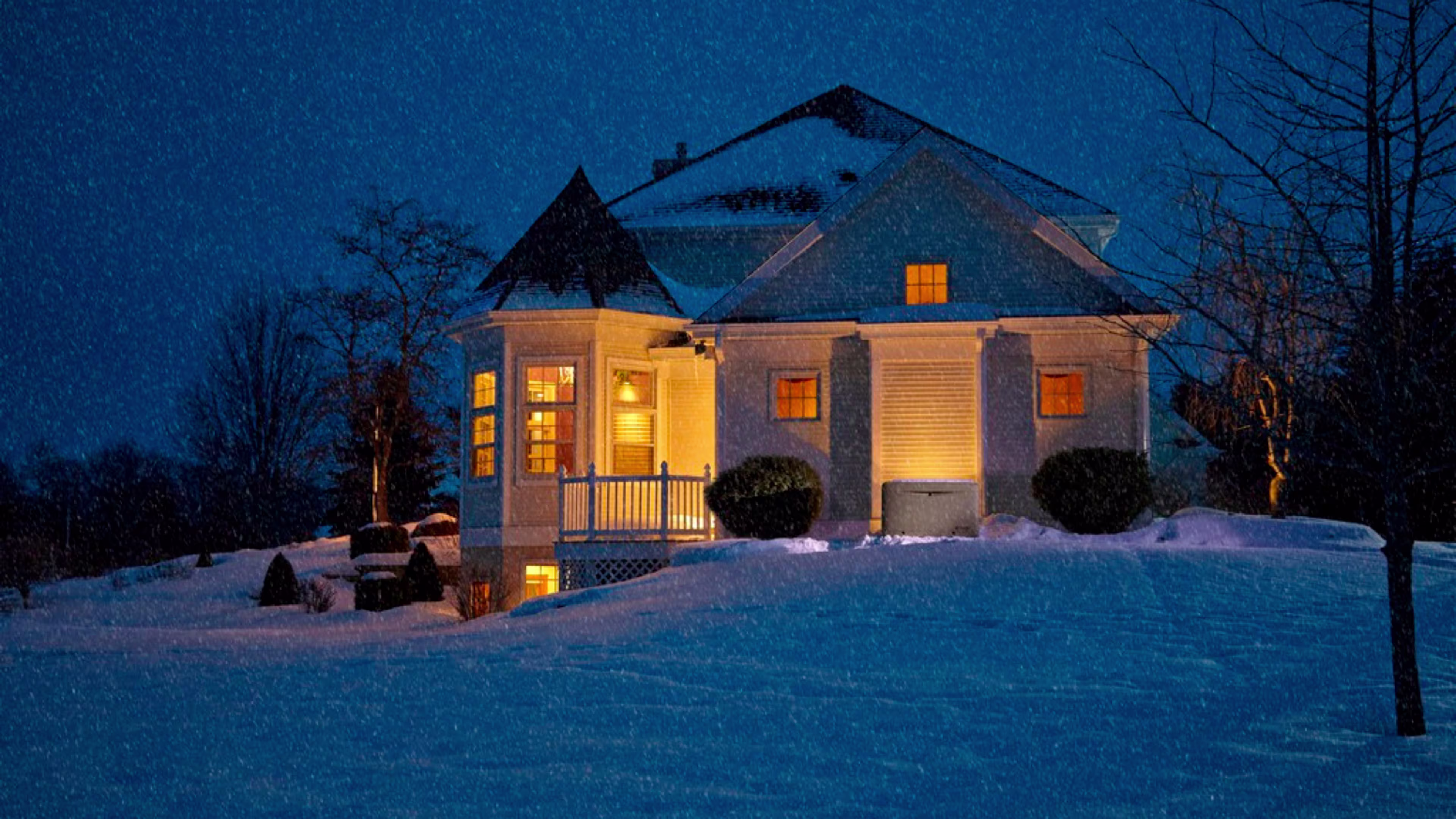 Image of a house with its light on at night in a snowy landscape.