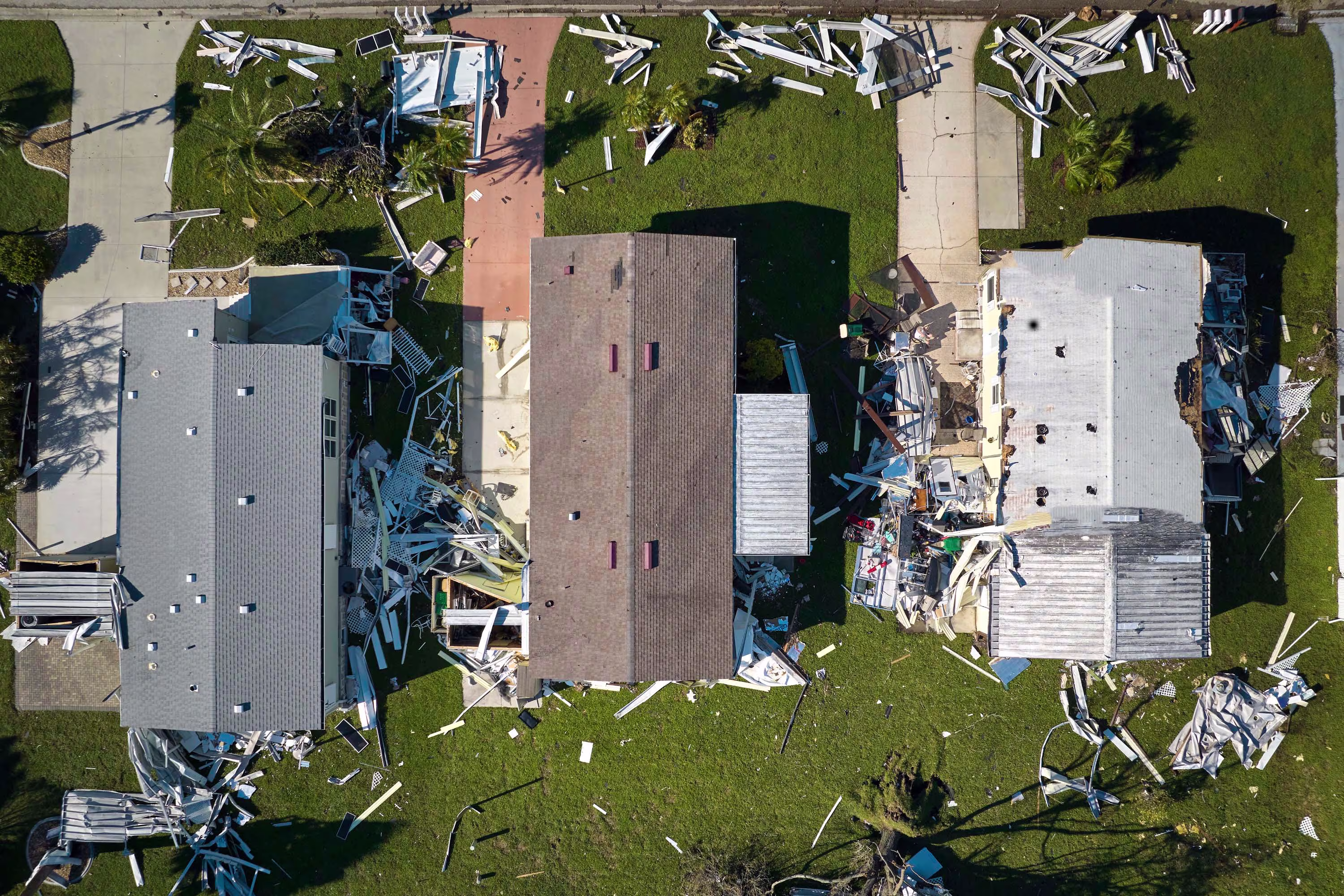Overhead view of three homes damaged by a storm with debris scattered throughout the yards.