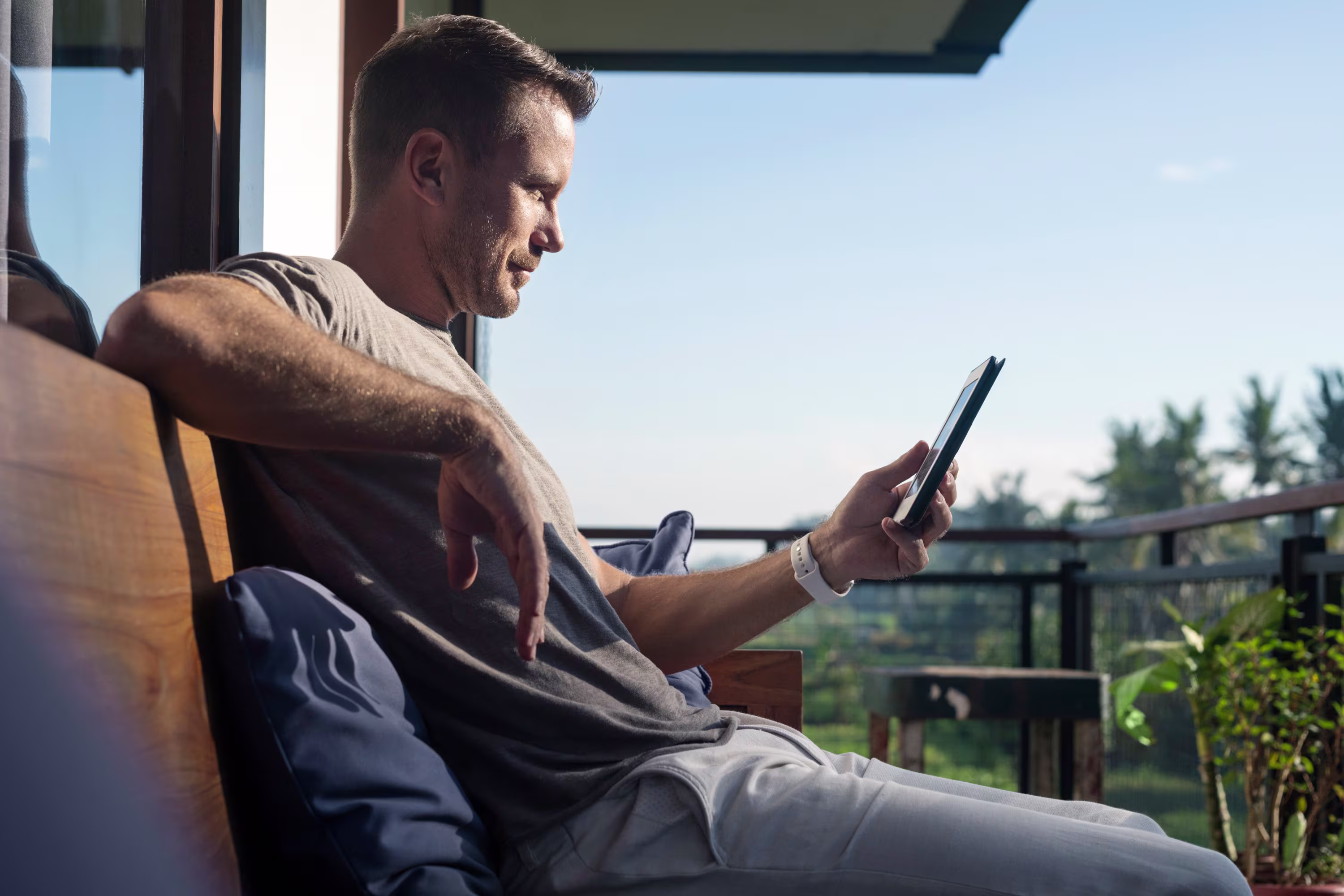 Image of a man sitting on a balcony looking at his phone with a green field outside