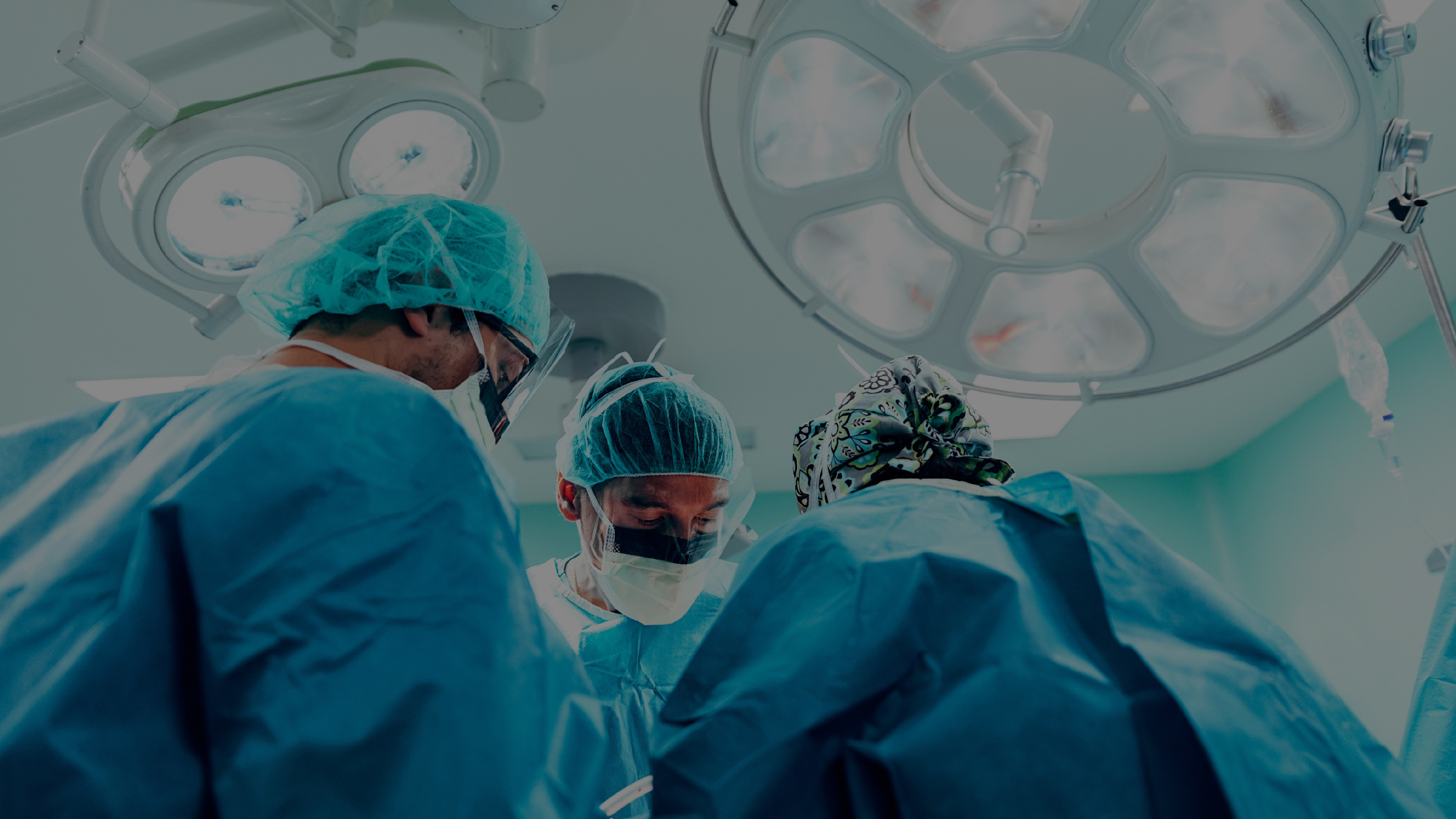 Three doctors wearing surgical scrubs, masks, and gloves, working together in an operating room.