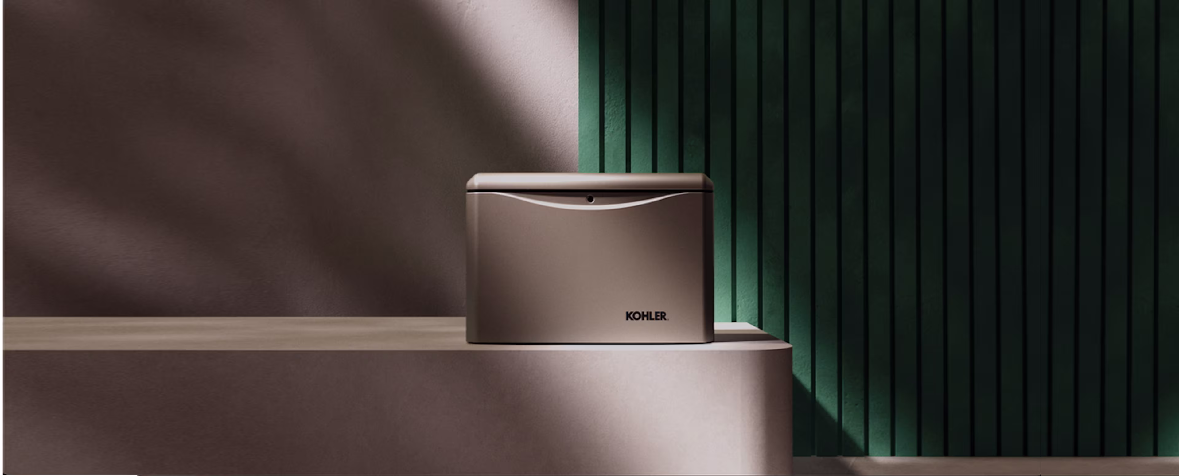Beige generator with Kohler logo placed on top of a step, against a wall half light grey and half dark green.