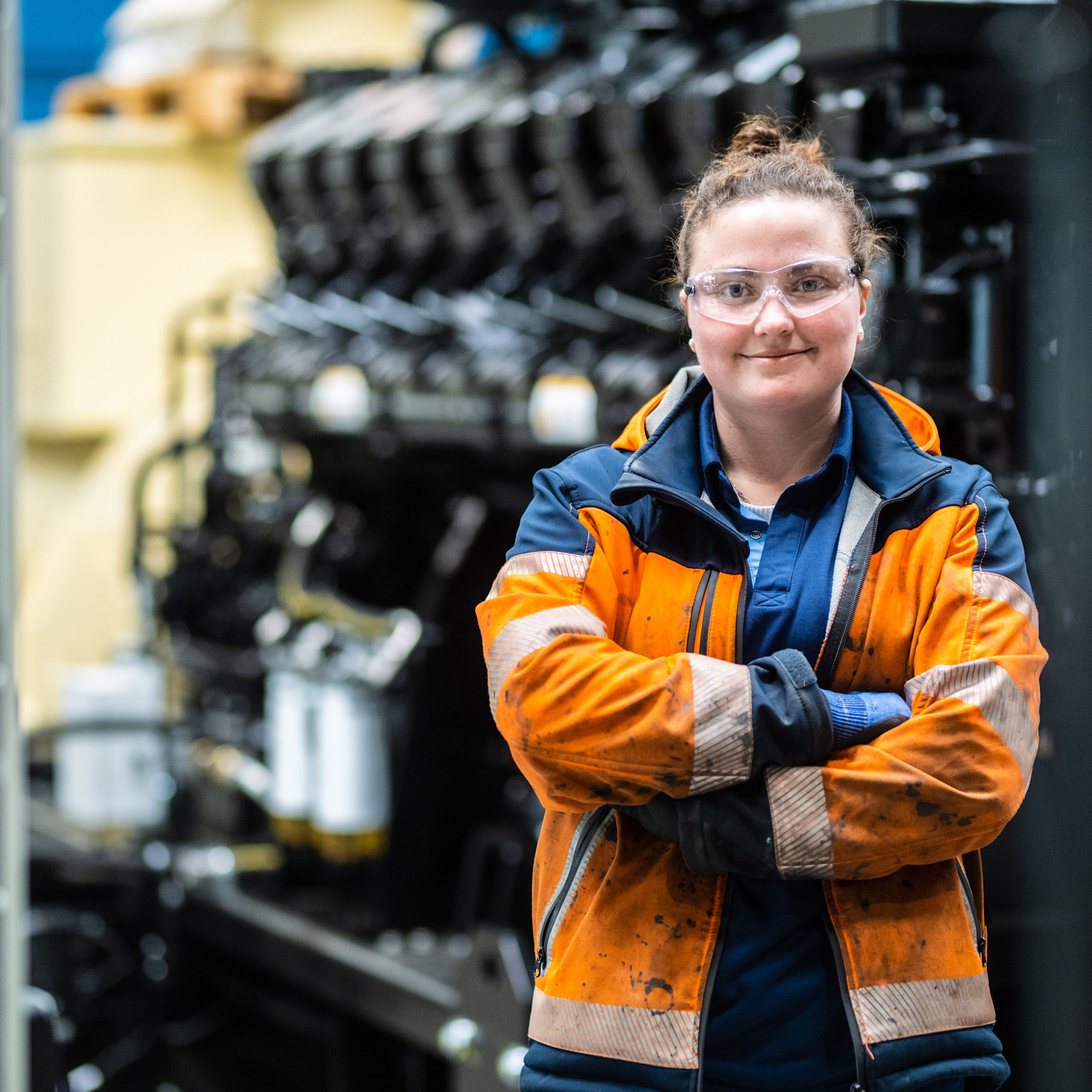 Woman in orange uniform with arms crossed in factory floor