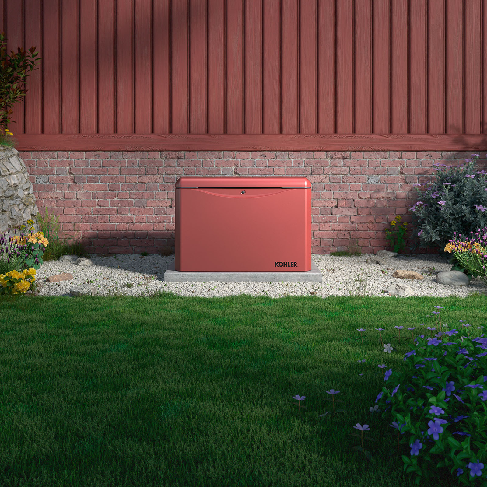 Image of a brick dust colored Kohler Home Generator sitting next to a house brick background on a cement base in a pebble area surrounded by a green lawn with bushes and flowers
