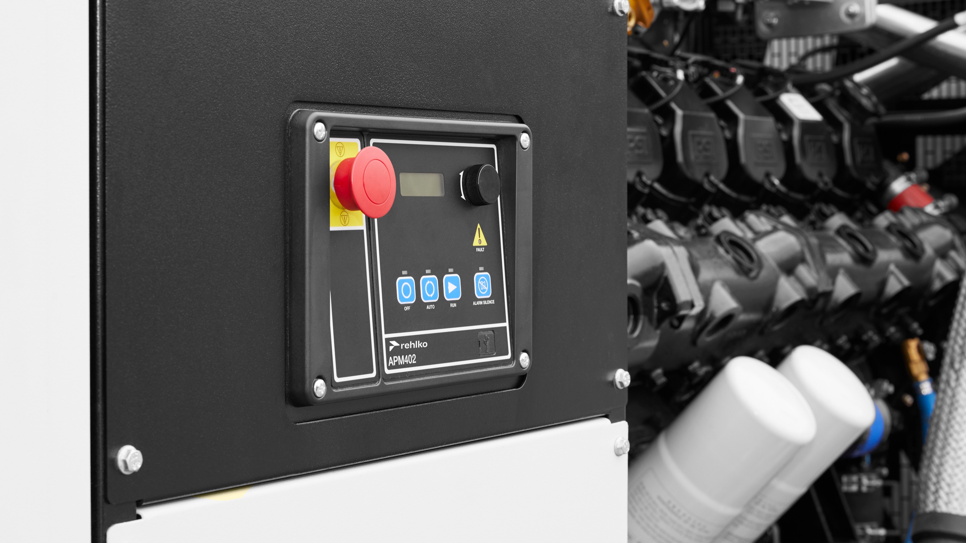 Rehlko APM 402 black controller installed in context, with a close-up view of its buttons and connected engine components.