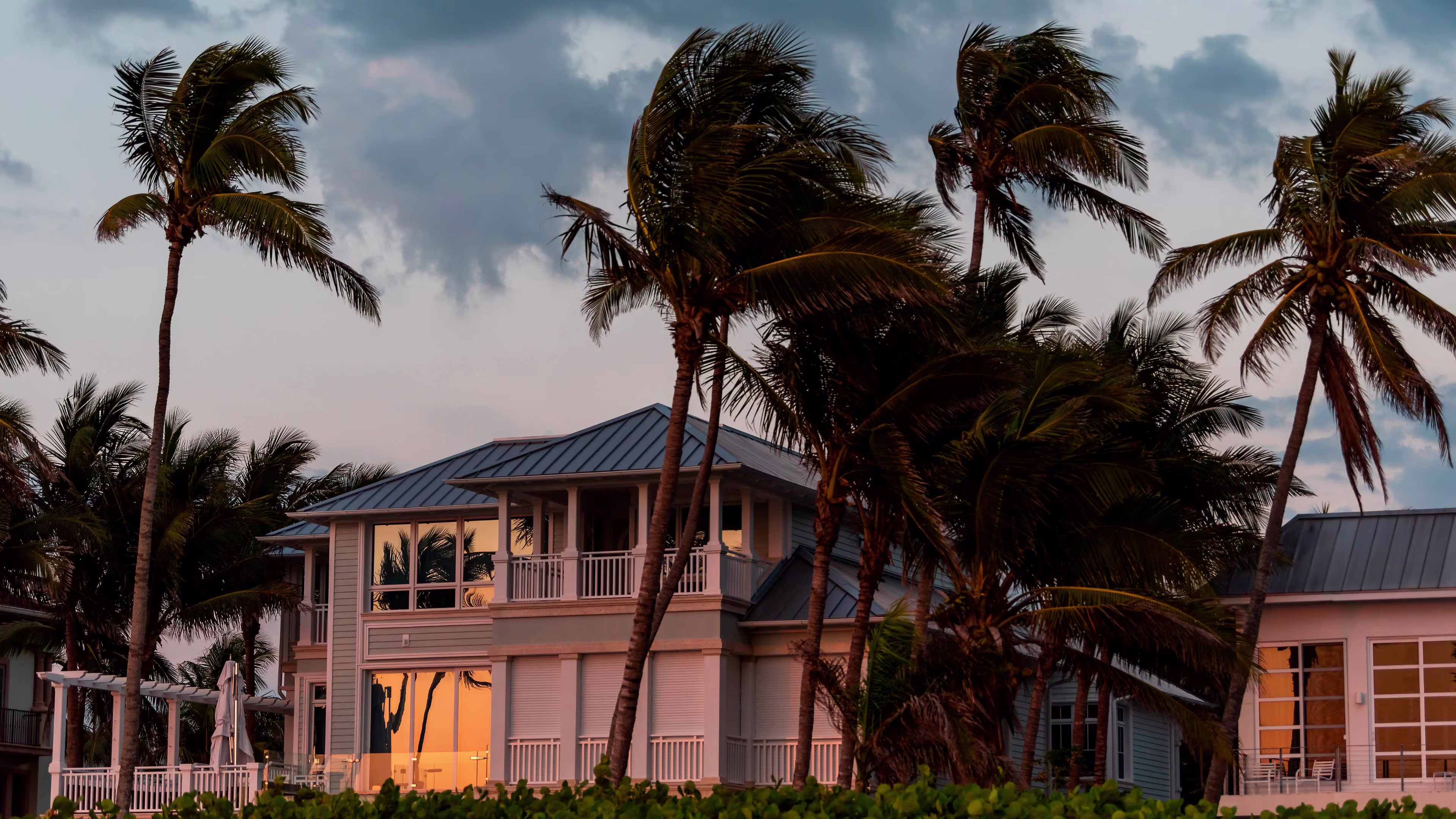 House with lights on, palm trees, wind, sunset