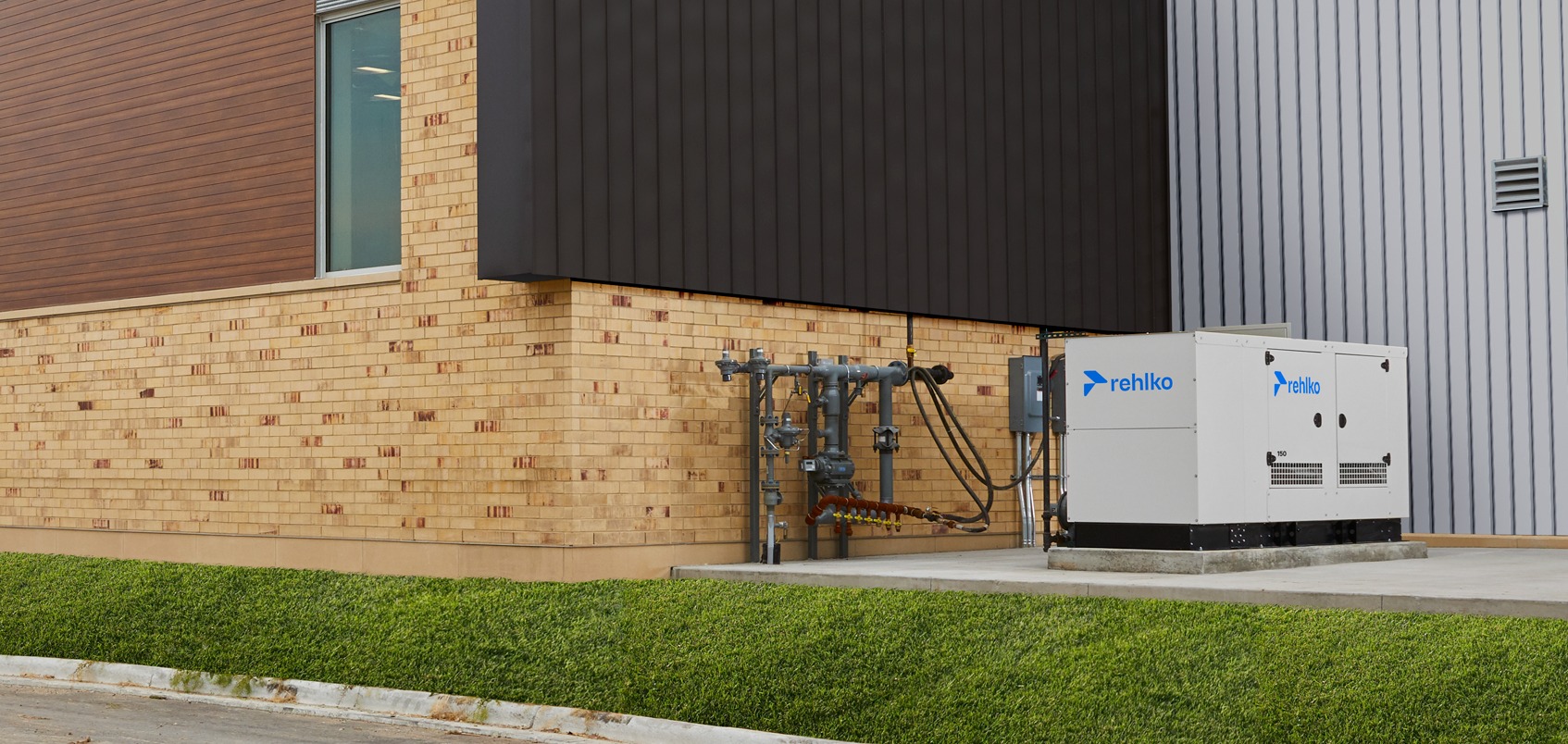 Outdoor gas generator positioned beside a complex of buildings under a foggy sky.