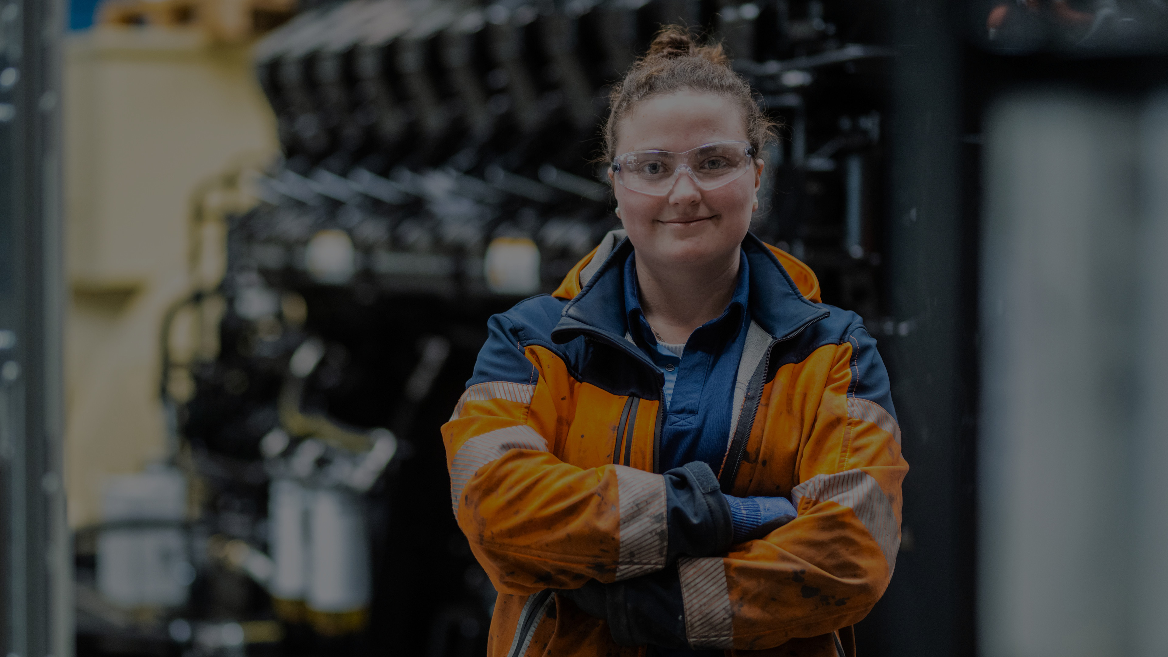 Woman in orange uniform with arms crossed in factory floor