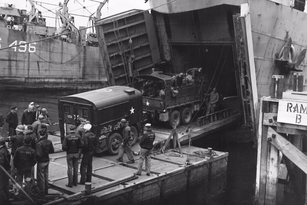Black and white photograph of US Navy team gathered on a dock while loading a ship with equipment.