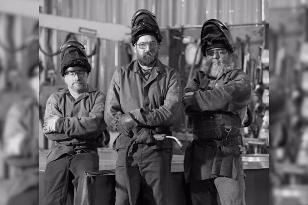 Black and white picture of three men wearing safety gear and looking into the camera.