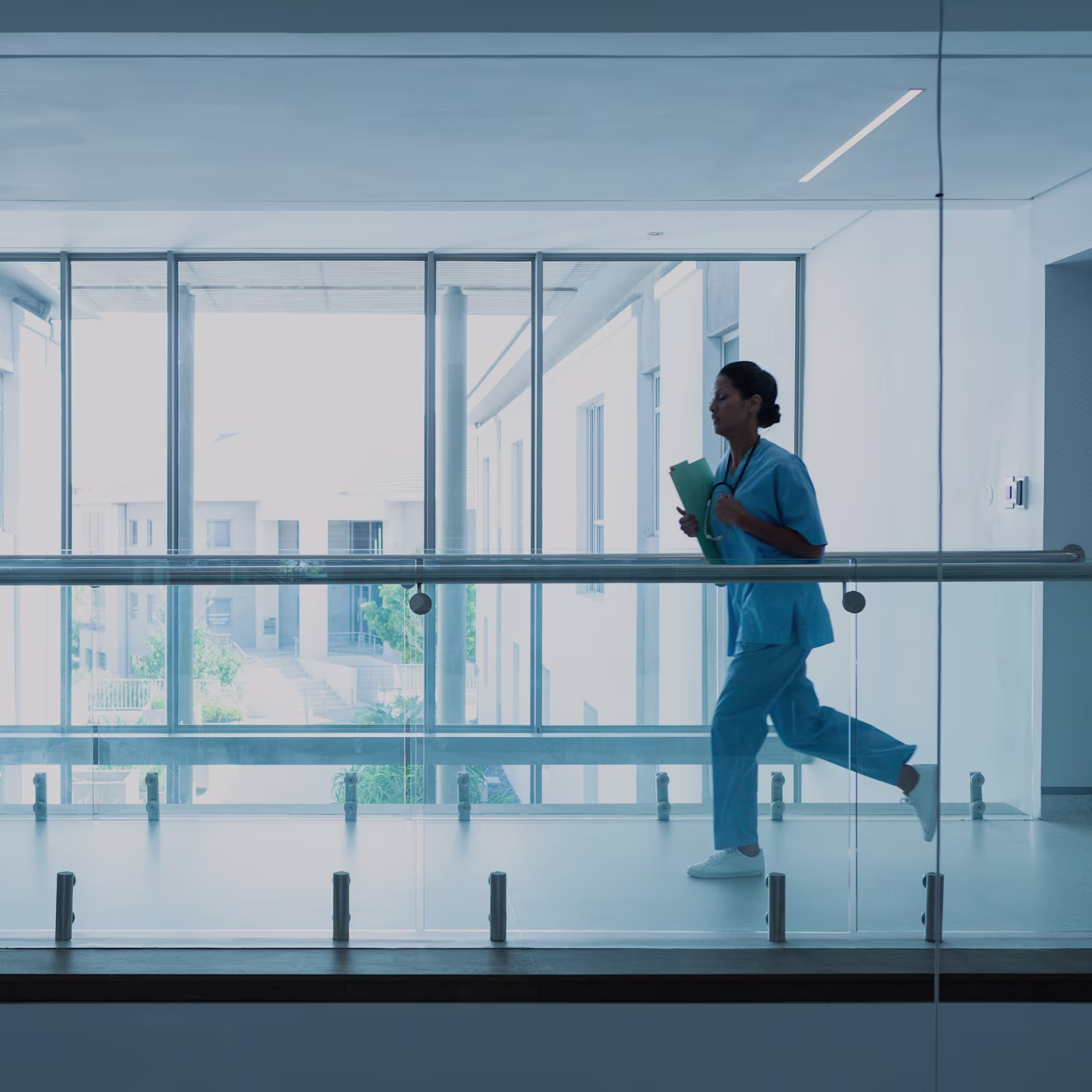 Woman in scrubs running inside a hospital building with all-glass windows