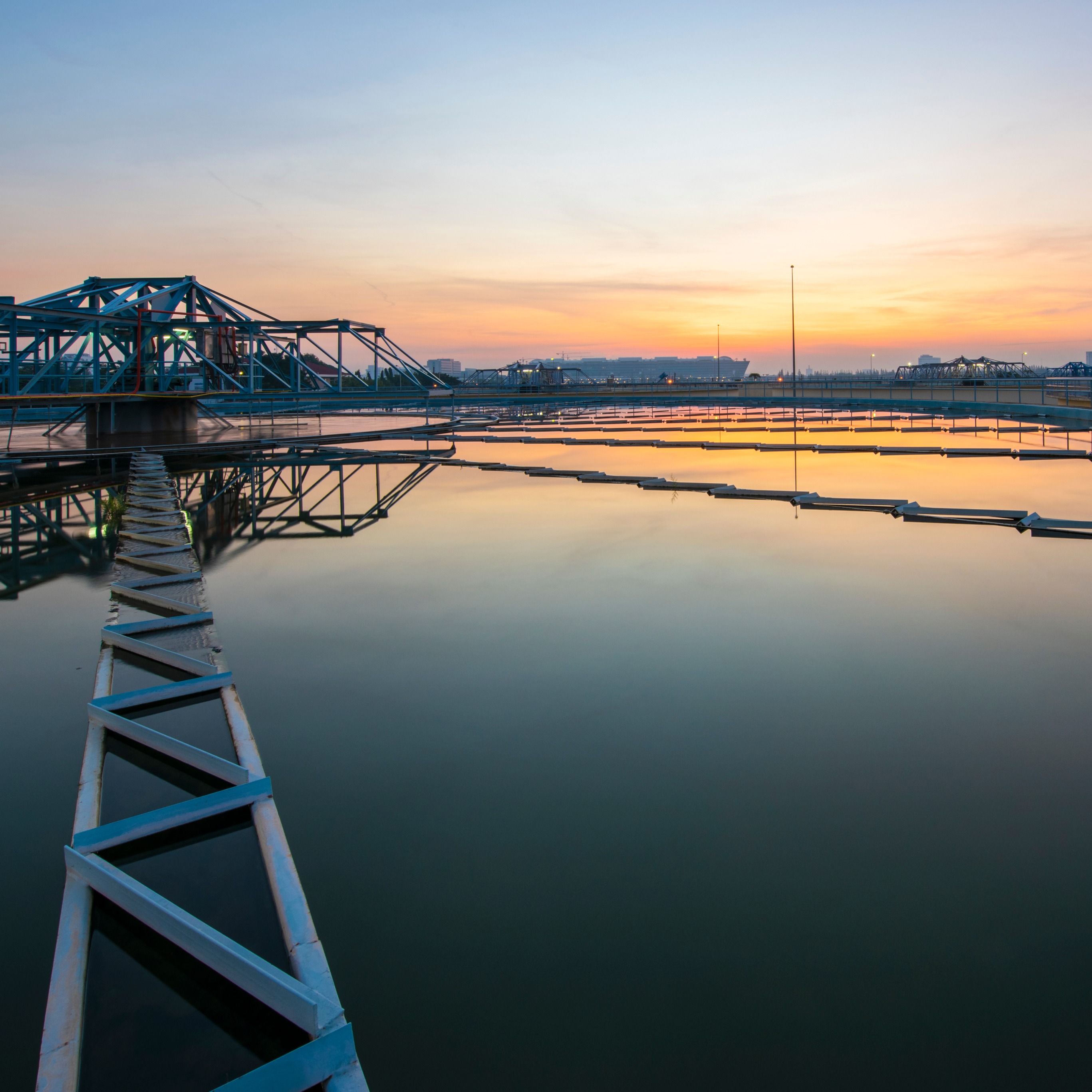 Water treatment reservoir at sunset with orange and pink sky reflections.