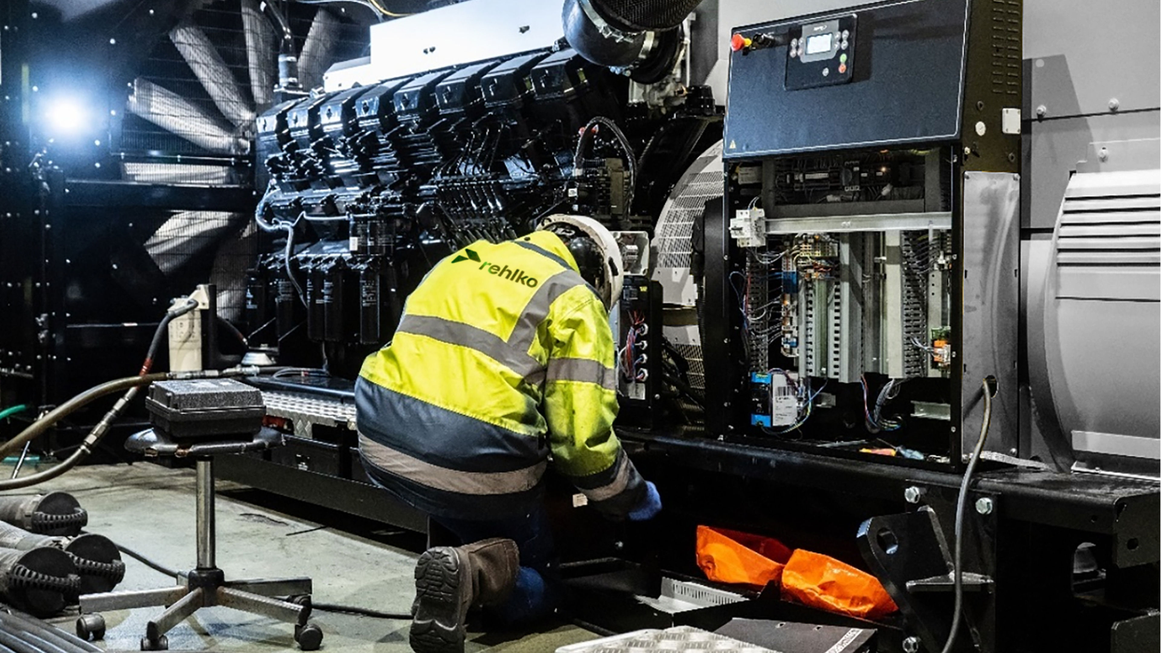 Man in safety jacket on his knees in front of a machine on a factory floor