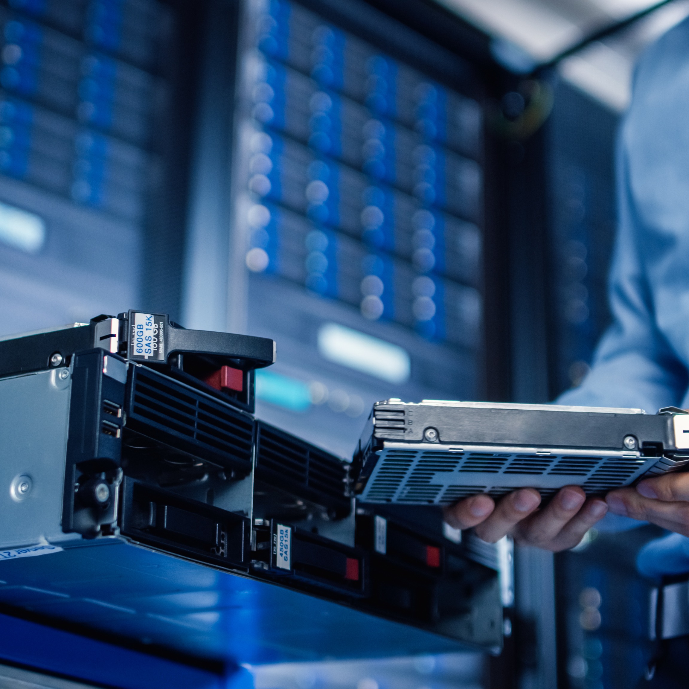 Blue-toned image of a man holding a hard drive inside a server room, surrounded by server racks and equipment.