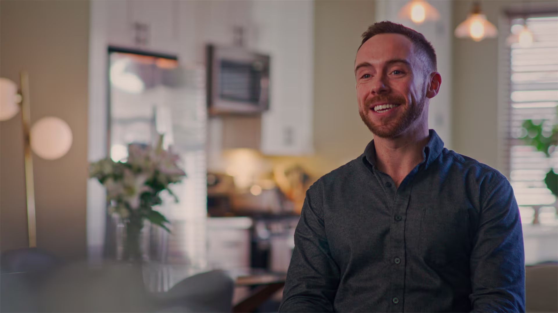 Man wearing dark shirt in a room with kitchen at the background