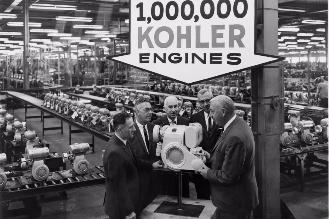 Black and white photography with five men around an engine inside a warehouse, with an arrow above saying "1,000,000 engines".