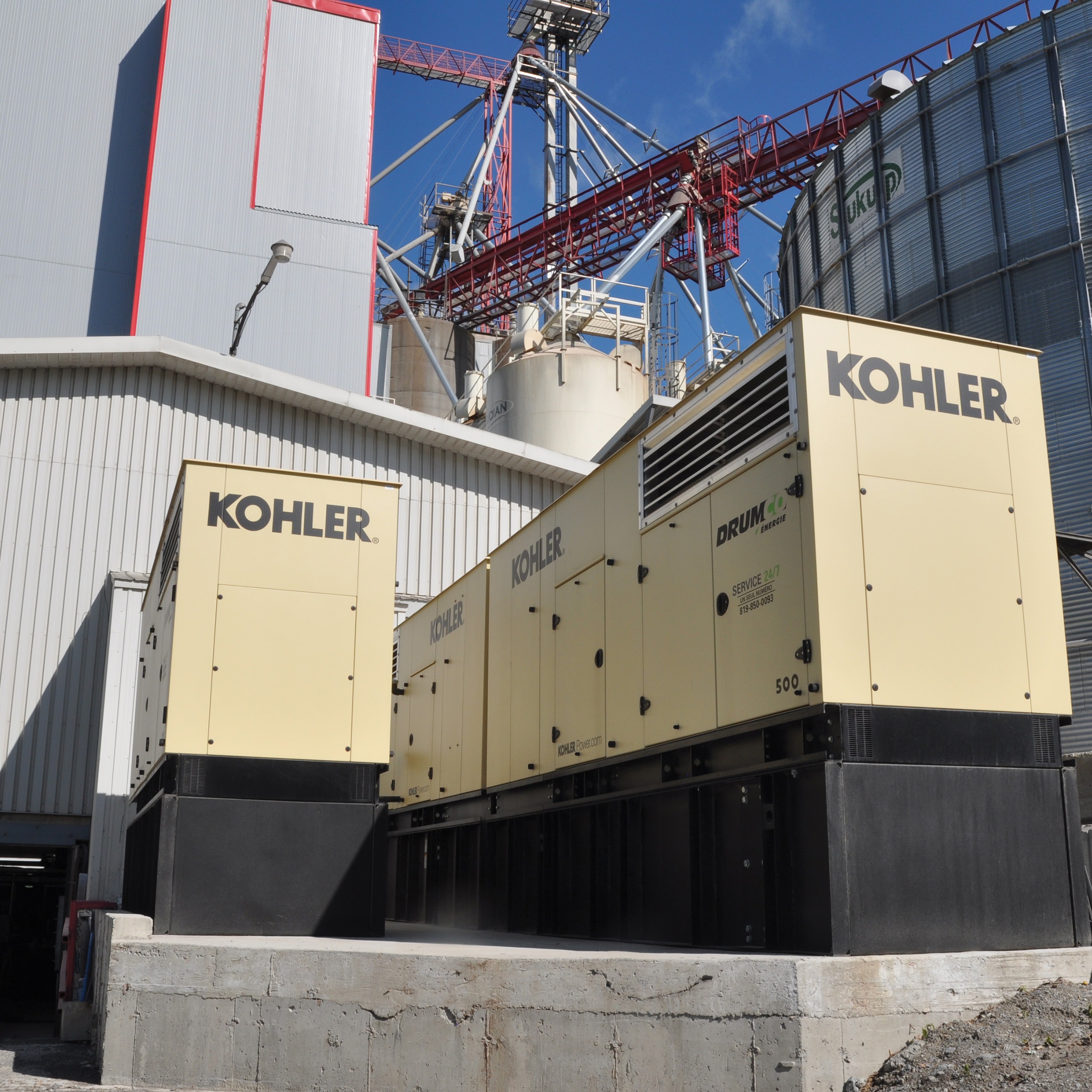 Two generators in different sizes, small and big outside a building.