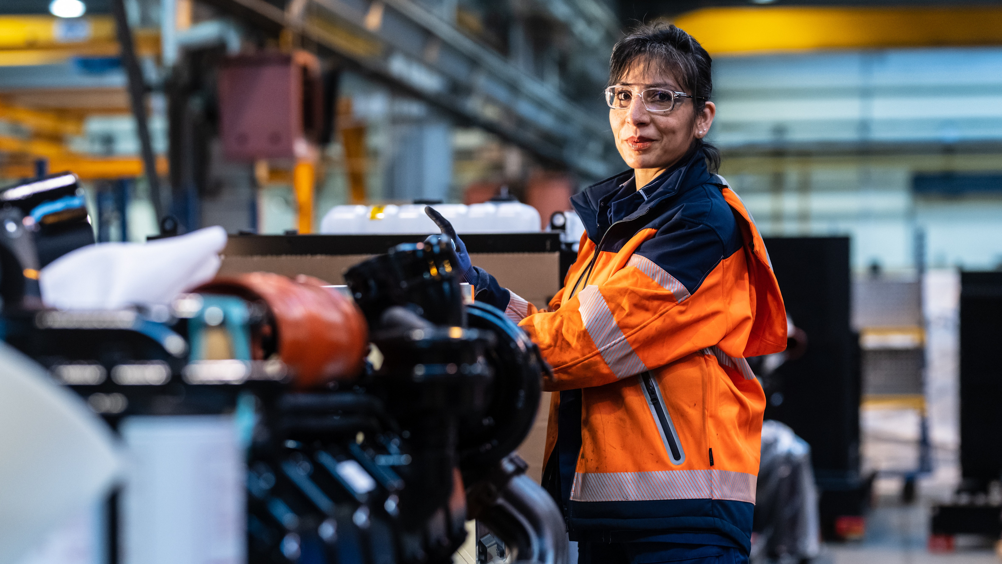 Woman in orange safety jacket in front of an equipment.