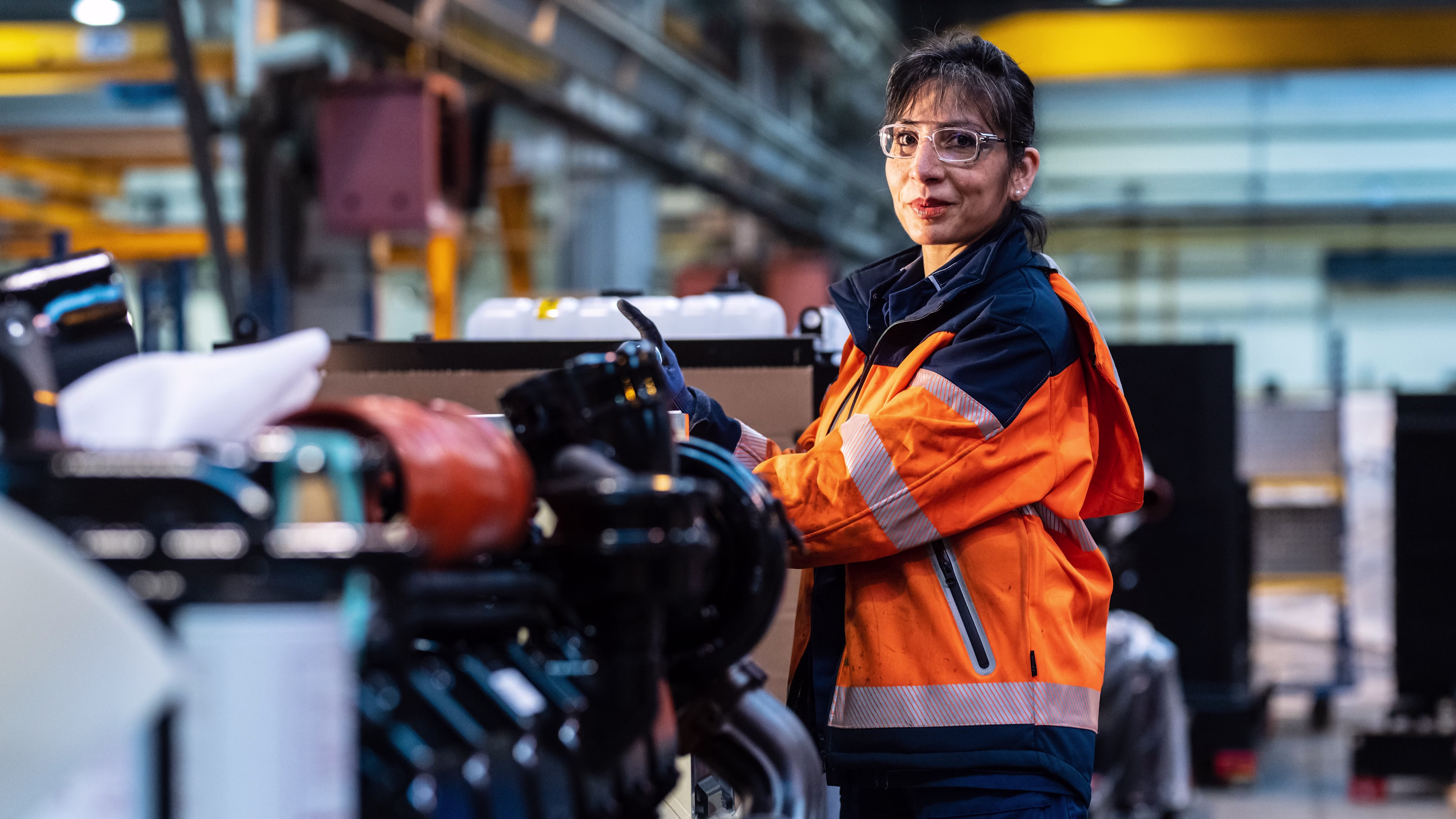 Woman in orange safety jacket in front of an equipment.