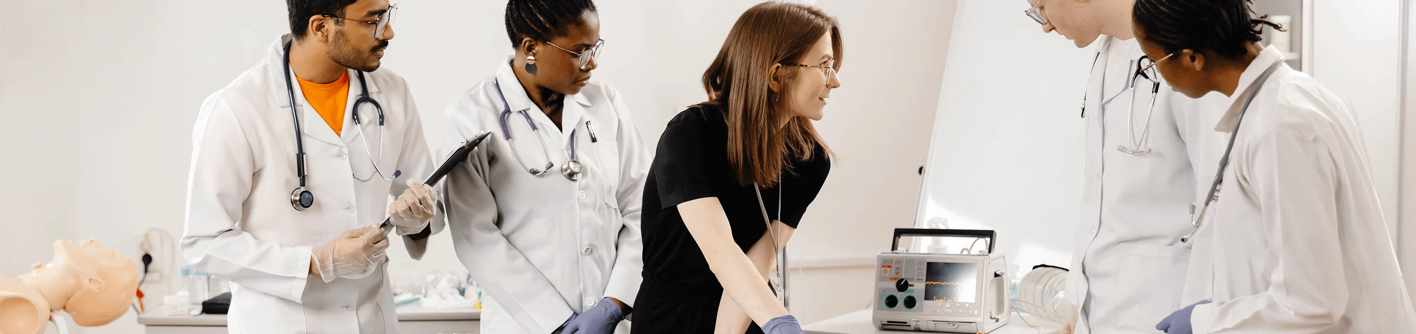 Medical students watch an instructor use a defibrillator on a training mannequin.
