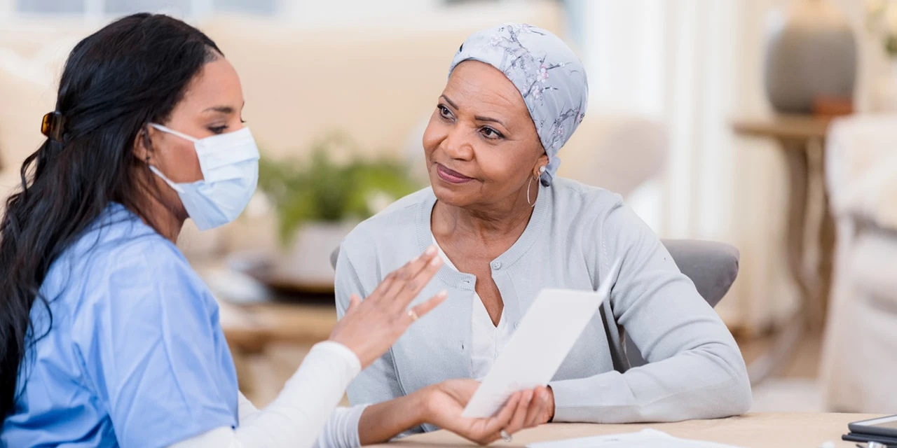 Woman with cancer listens carefully to nurse wearing protective mask (SDI Productions/E+ via Getty Images)