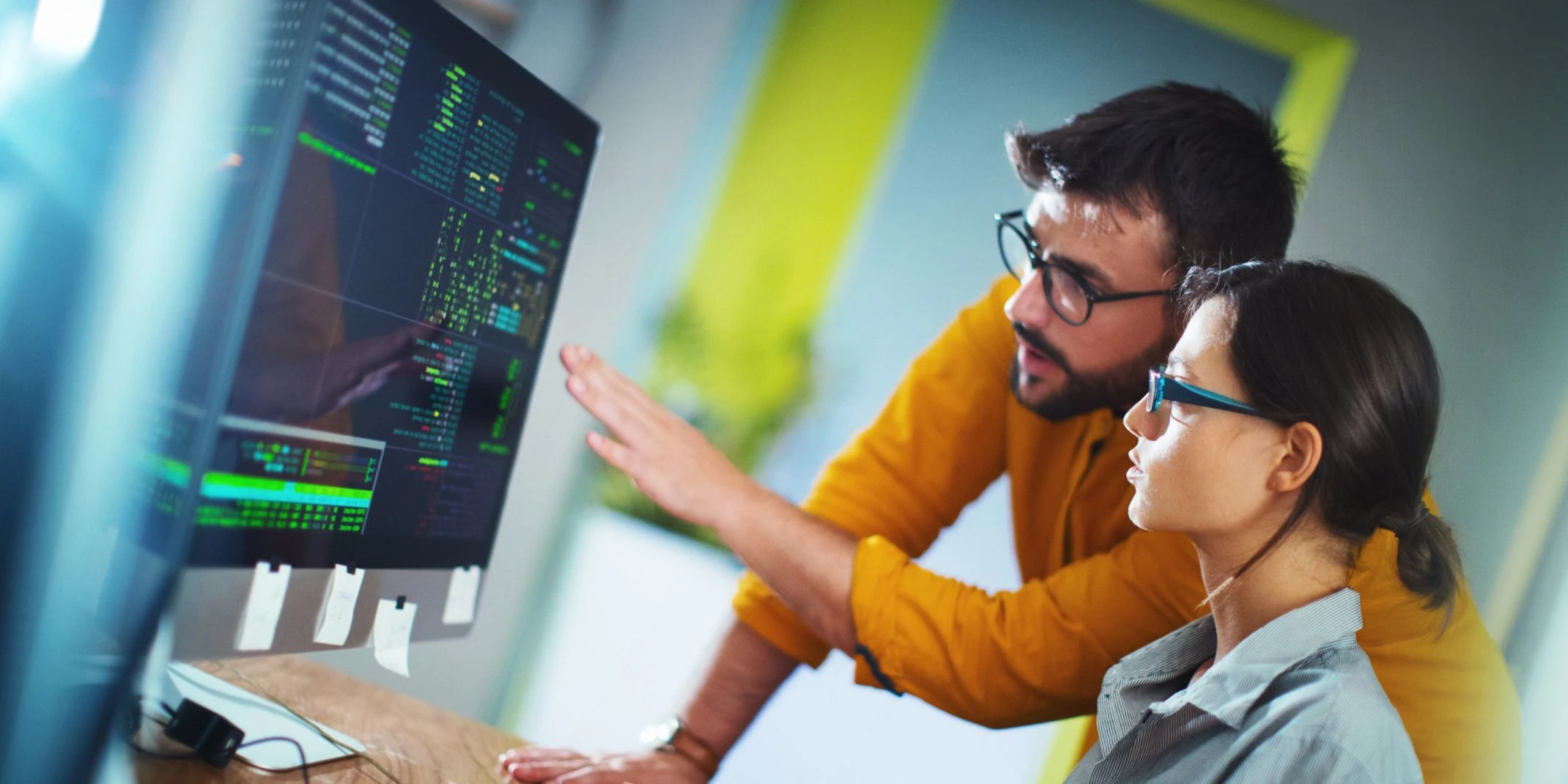 Closeup side view of couple of mid 20's software developers resolving some issues with the code they're currently working on.