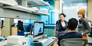 Group of scientists chat around desk, in the lab