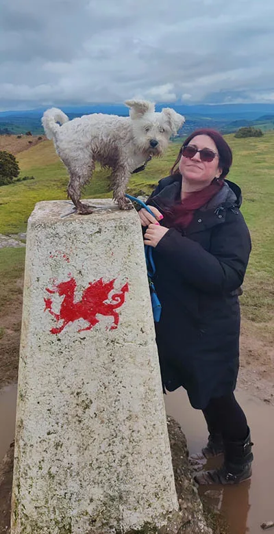 Photo of Catrina Scott with her dog Maybe at Twyn-Y-Gaer Hillfort Trig Point in Wales.