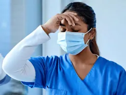 A south Asian woman rests her hand on her forehead against the glass, looking distressed.