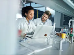 Photo depicting two pharmaceutical researchers working at a computer. (Source: skynesher/E+ via Getty Images)